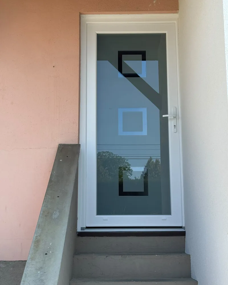 Porte d’entrée blanche à grand vitrage décoré de carrés, en haut d’un escalier — photo de chantier